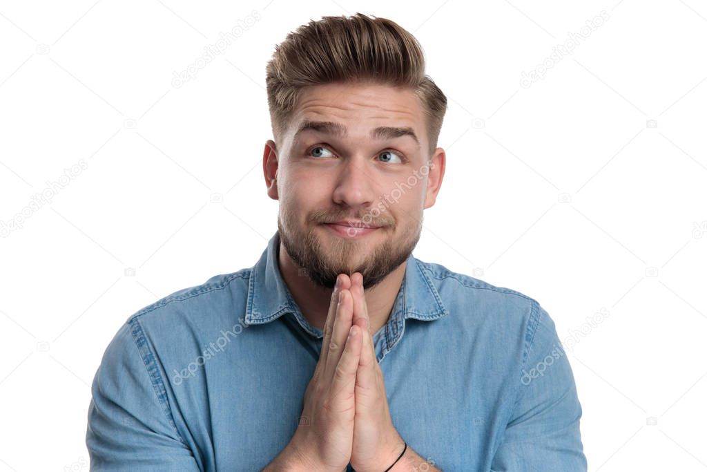 Positive casual man praying and looking up while wearing shirt, standing on white studio background
