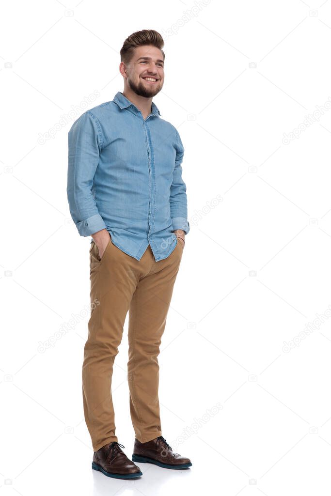 Happy casual man smiling with his hands in his pockets while standing on white studio background