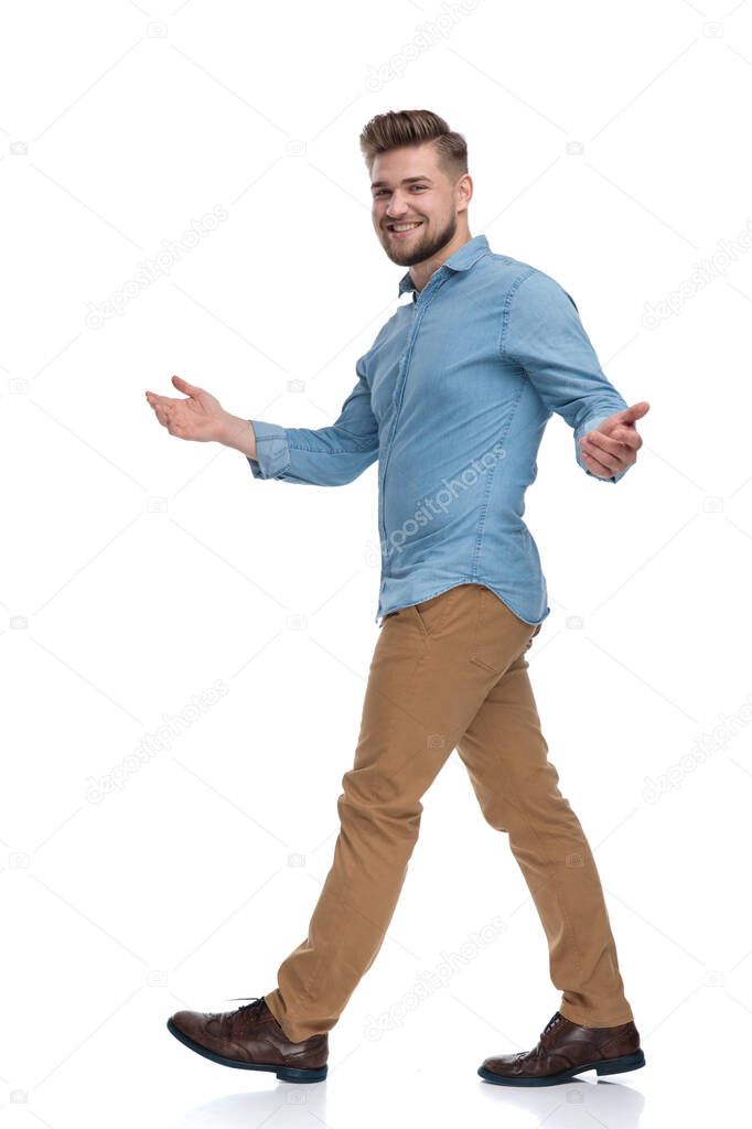 Side view of a friendly casual man welcoming and laughing while walking on white studio background