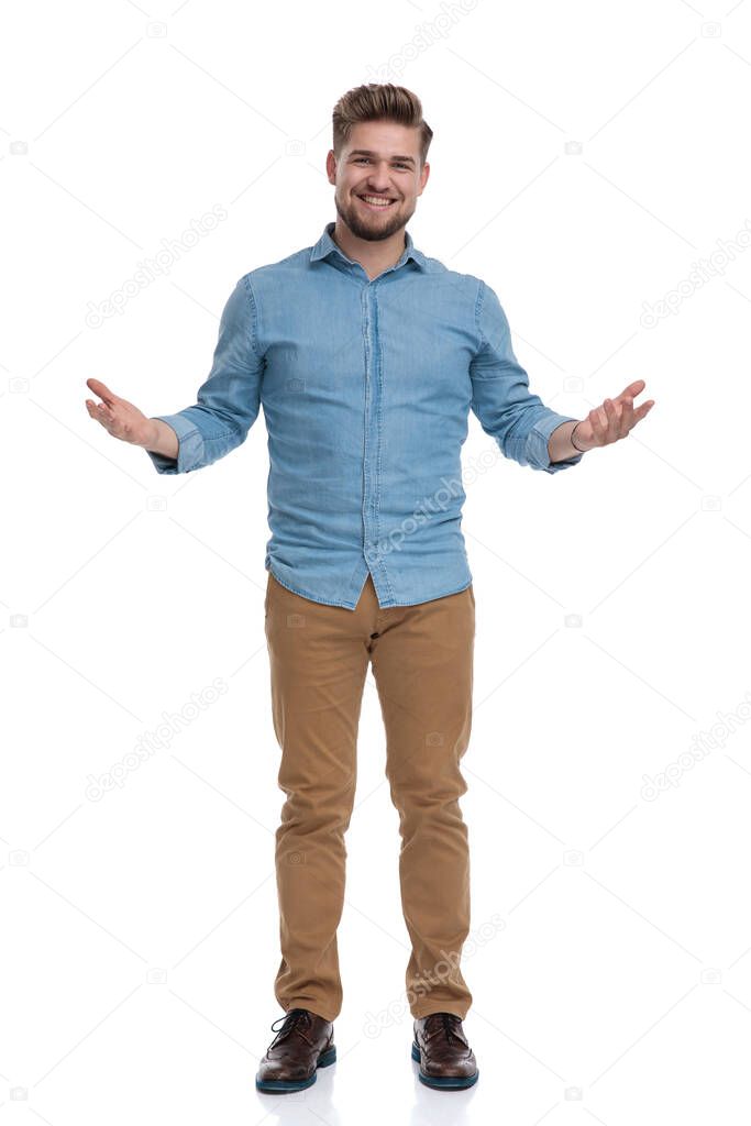 Cheerful casual man welcoming and smiling with his hands wide open while standing on white studio background
