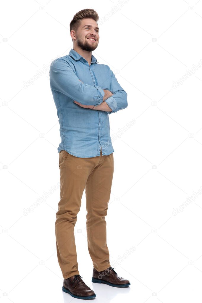 Hopeful casual man looking away with his hands crossed at his chest while standing on white studio background