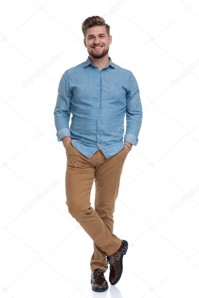 Happy casual man holding both hands in his pockets and smiling while standing on white studio background