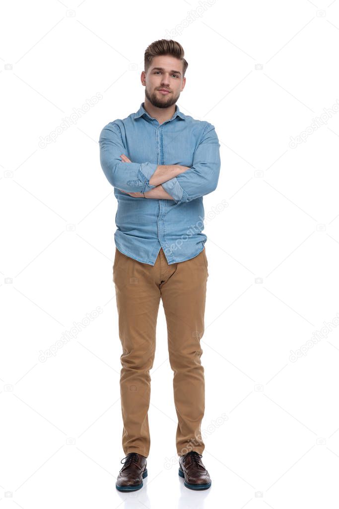 Serious casual man holding his hands folded at his chest while standing on white studio background
