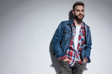 Motive olmuş bir manken, gri stüdyo arka planında dikilirken iki elini de cebinde taşıyor.