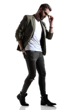 Merak eden bir manken güneş gözlüğünü ayarlıyor ve elini arka cebinden tutuyor, beyaz stüdyo arka planına basıyor.