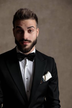 Sıkıcı damat smokin giyer ve duvar kâğıdı stüdyo arka planında bir tabureye oturur.