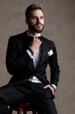 Ciddi damat papyonunu düzeltip smokin giyerken ve duvar kâğıdı stüdyo arka planında bir taburede otururken gözlerini kaçırıyor.