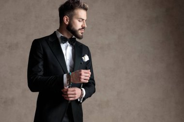 Dalgın damat smokin giyerken ve duvar kâğıdı stüdyo arka planında dikilirken kolunu ayarlıyor ve başka tarafa bakıyor.