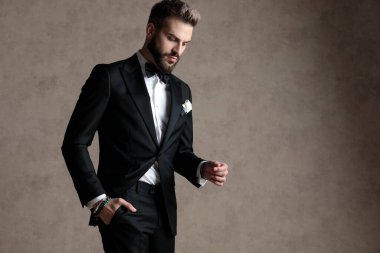 Smokin giyerken elini cebinde tutan düşünceli damat ve stüdyo arka planında yürüyen.