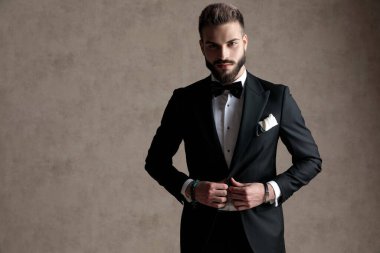 Smokin giyerken ceketini düzelten ve arka planda duran kendine güvenen damat.