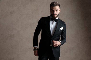 Smokin giyerken ve duvar kâğıdı stüdyo arka planında dururken kendine güvenen damat poz veriyor.