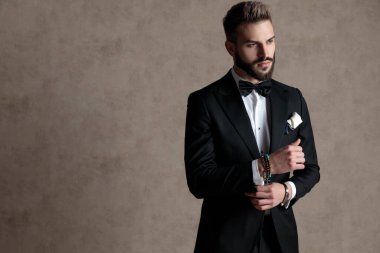 Kendine güveni olan damat smokin giyerken ve duvar kâğıdı stüdyo arka planında dikilirken kolunu düzeltip gözünü kaçırıyor.