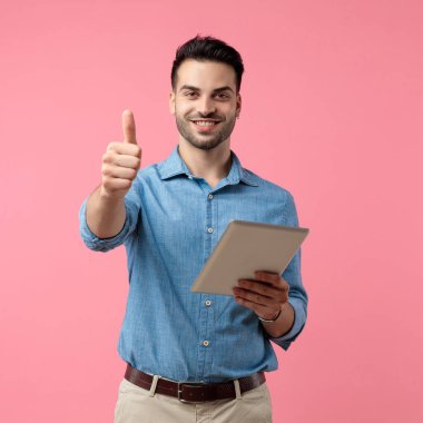 Genç, sıradan bir adam, baş parmak işareti yapıyor ve sekmeyi tutuyor, pembe arka planda duruyor. 