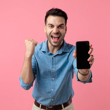 Siyah boş ekran gösteren genç bir adam zaferi kutluyor, pembe arka planda duruyor.