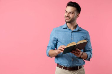 Genç, sıradan bir adam elinde kitabı tutuyor ve pembe arka planda duruyor.
