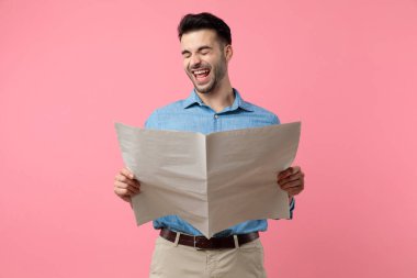 Mutlu genç adam gazete okuyor ve gülüyor, pembe arka planda duruyor.