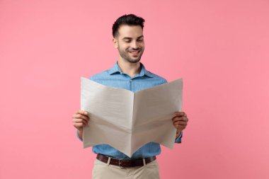 Mutlu genç adam gazete okuyor ve gülümsüyor, pembe arka planda duruyor.