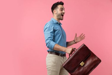Elinde bavul tutan ve zaferi pembe arka planda kutlayan mutlu genç adam.