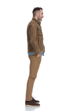 Deri ceket giyip beyaz stüdyo arka planında dururken iki elini de cebinde tutan yakışıklı bir adamın yan görüntüsü.