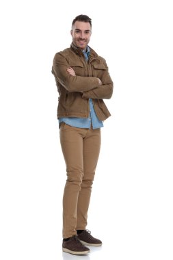 Deri ceket giyip beyaz stüdyo arka planında dururken elleri göğsünde çapraz gülümseyen mutlu sıradan bir adam.