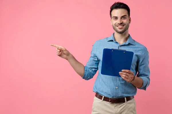 Jovem Feliz Segurando Prancheta Apontando Dedo Para Lado Fundo Rosa — Fotografia de Stock