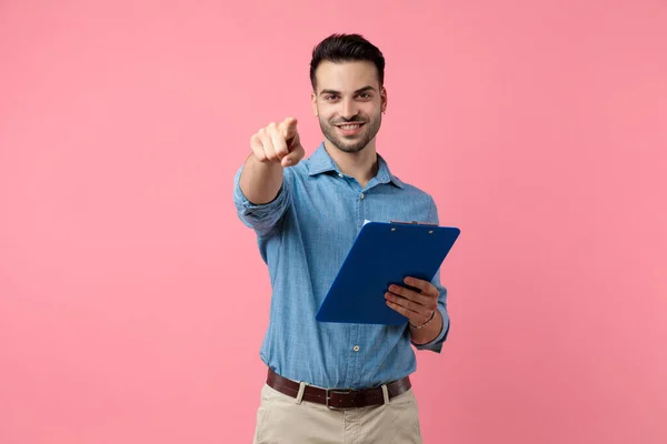 Lächelnder Junger Lässiger Typ Mit Klemmbrett Und Zeigefinger Stehend Auf — Stockfoto