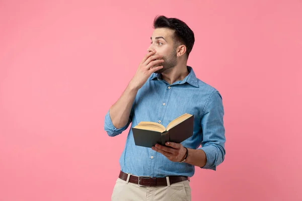 カジュアルな男が本を読んで手をつないでピンクの背景を見ながら — ストック写真