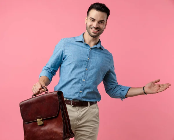 Joven Chico Casual Sosteniendo Maleta Presentando Lado Sonriendo Sobre Fondo —  Fotos de Stock