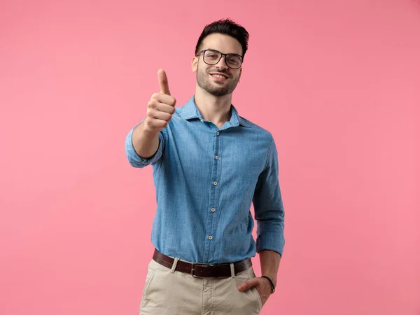 デニムシャツを着た若いカジュアルな男が笑顔でピンクを背景に親指を立てる — ストック写真
