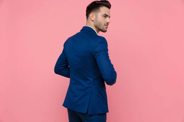 一个穿着蓝色西服 站在粉红工作室背景上的迷人商人的背影 — 图库照片