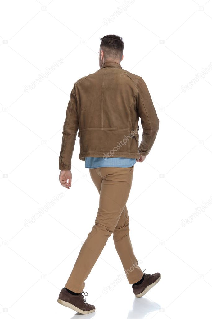 Rear view of a eager casual man wearing a leather jacket while walking on white studio background