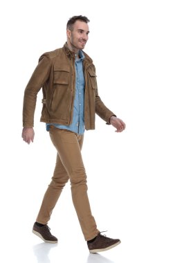 Deri ceket giyerken gülümseyen ve beyaz stüdyo geçmişine basan kendinden emin bir adam.