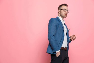 Hevesli, zeki, sıradan bir adam, eli cebinde, gözlük takmış ve pembe stüdyo arka planına basmış bir şekilde başka tarafa bakıyor.