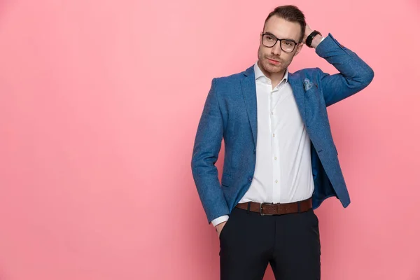时尚聪明的休闲男人手牵着头和口袋 戴着眼镜 站在粉红的工作室背景上 — 图库照片