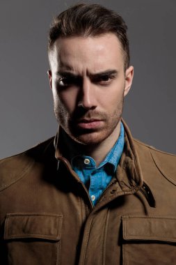 Sert manken, deri ceket giyerken ve arka planda gri duvar kâğıdının üzerinde dururken ciddi bir şekilde ileriye bakıyor.