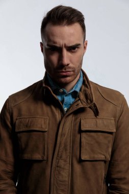 Deri ceket giyerken ve arka planda gri duvar kâğıdının üzerinde dikilirken kaşlarını çatmış ve ileriye bakıyordu.