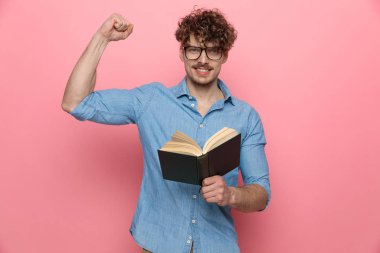 Kendine güvenen genç adam kitabı tutuyor ve kaslarını gösteriyor, pembe arka planda duruyor.