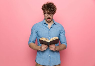 Kot gömlekli, kitap okuyan ve pembe arka planda duran etkileyici genç adam.