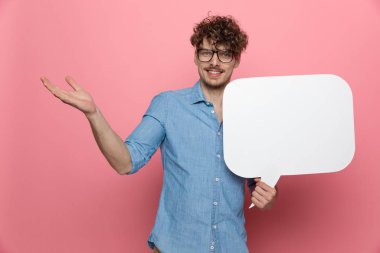 Genç mutlu adam konuşma balonunu tutuyor ve pembe arka planda duruyor.