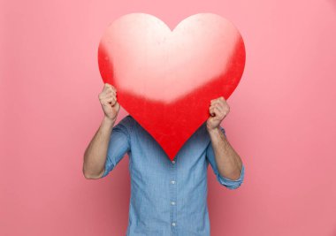 Büyük kırmızı kalpli kot giyen, pembe arka planda duran sıradan bir genç.