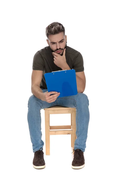 Curioso Hombre Casual Leyendo Desde Portapapeles Con Mano Barbilla Mientras — Foto de Stock