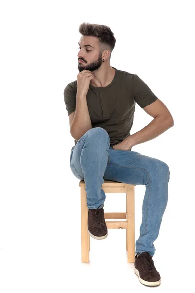 Ciekawy Swobodny Mężczyzna Odwraca Wzrok Ręką Podbródku Siedząc Krześle Białym — Zdjęcie stockowe