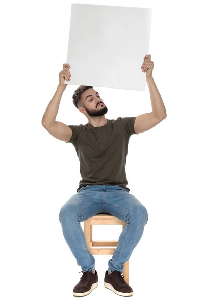 Lässiger Mann Der Wegschaut Und Eine Leere Plakatwand Hält Sitzt — Stockfoto