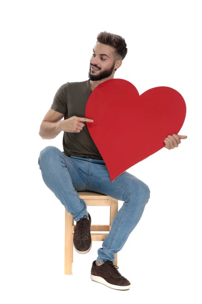 Hombre Casual Positivo Apuntando Sosteniendo Corazón Mientras Está Sentado Una — Foto de Stock