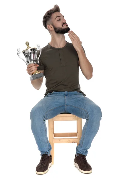 坐在白色画室背景的椅子上 傲慢而随意的男人拿着奖杯 摸着下巴 — 图库照片