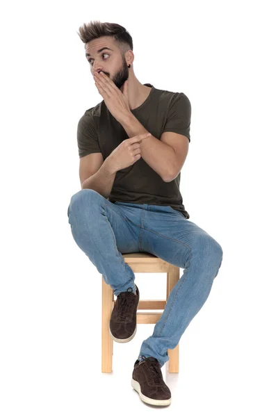 Młody Swobodny Mężczyzna Zakrywający Usta Wskazujący Plotkujący Siedząc Krześle Białym — Zdjęcie stockowe