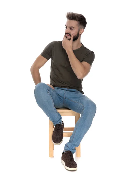 自信を持ってカジュアルな男彼の顎に手を保持し 離れて見ながら 白いスタジオの背景に椅子に座って — ストック写真