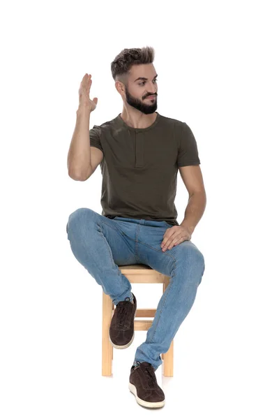 白いスタジオの背景にある椅子に座っている間に一人で残されるために手を振っカジュアルな男 — ストック写真