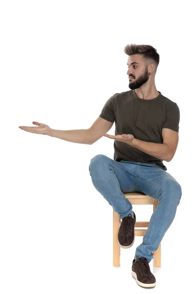 Incomodado Homem Casual Apresentando Explicando Enquanto Sentado Uma Cadeira Fundo — Fotografia de Stock