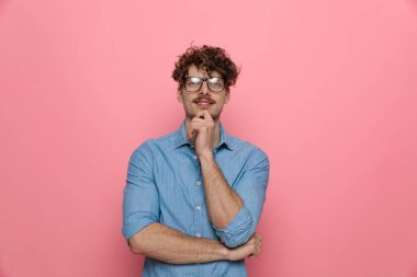 Gülümseyen genç adam el ele tutuşuyor ve düşünüyor, pembe arka planda duruyor.